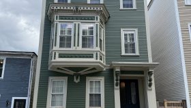 3 story wood clapboard house with side hall entry, flat roof and prominent second story oriel window