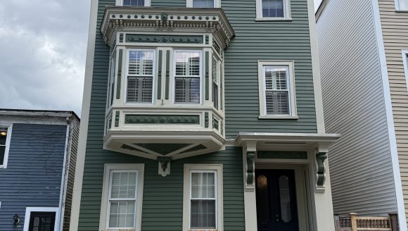 3 story wood clapboard house with side hall entry, flat roof and prominent second story oriel window