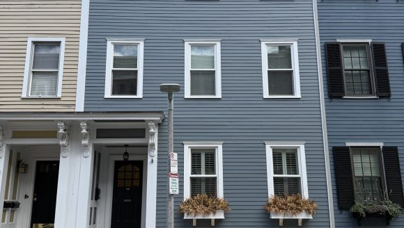 3 story wood clapboard house with flat roof and brick foundation